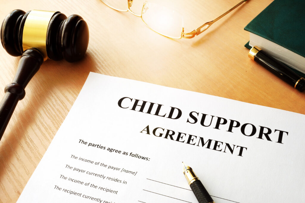 Gavel, eyeglasses, a green book, and a pen on a desk beside a document titled 'CHILD SUPPORT AGREEMENT'